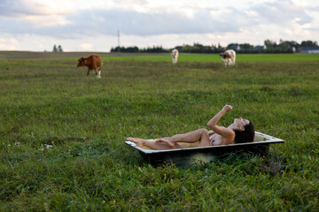 A Beautiful Woman Relaxing in Nature’s Bathtub, Surrounded by Grazing Cows at Dusk