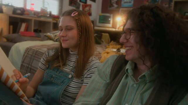 Chest up shot of cheerful carefree teenage couple having fun at home after school, girl blowing bubble gum and guy with soda can laughing while doing homework together in bedroom, 90s aesthetics
