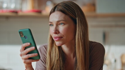 Portrait woman looking mobile phone at kitchen. Attractive lady surfing internet