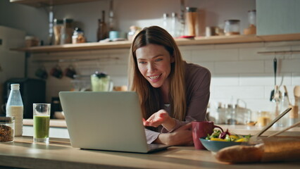 Fototapeta premium Happy girl video calling laptop at home kitchen close up. Smiling woman talking
