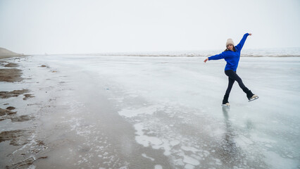 Caucasian woman in a blue sweater is skating on a frozen lake. The figure skater performs the program.