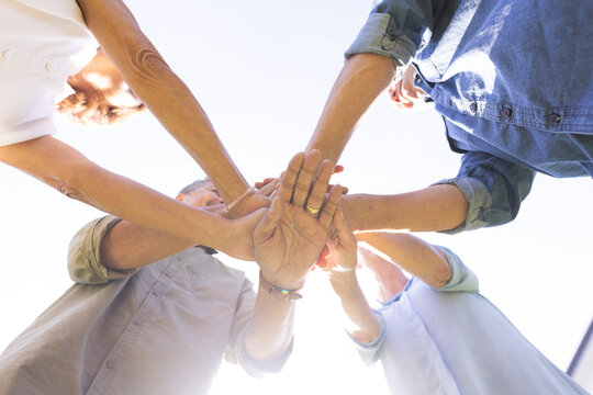 Senior diverse friends joining hands in unity, showing teamwork and friendship, at home