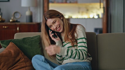 Joyful woman talking mobile phone relaxing at home couch. Smiling girl gossiping