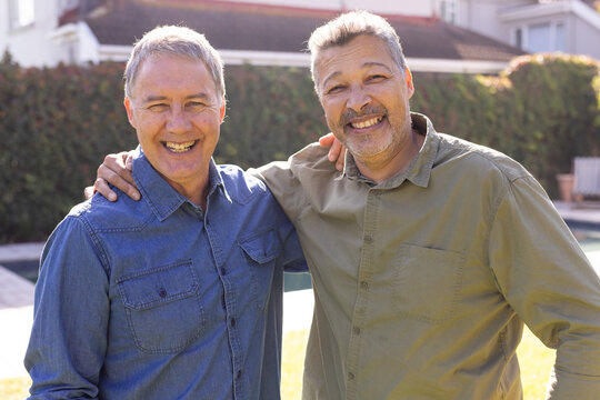 Smiling senior diverse friends standing outdoors, enjoying time together in backyard, at home