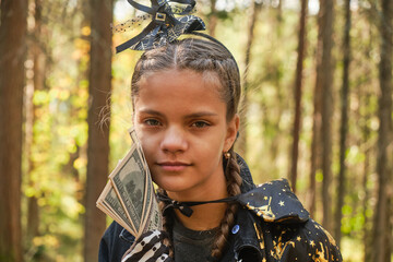 dark skinned teenage girl dressed as witch or wizard counts and plays with money, trick or treat concept, halloween earnings