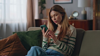 Stressed girl looking cellphone screen reading bad news at couch. Upset woman