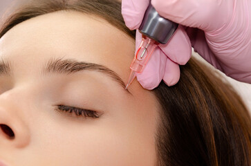 Young woman getting eyebrow permanent makeup in beauty salon.