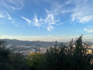 Fototapeta premium Barcelona Cityscape from Above at Dusk: A panoramic view of Barcelona’s urban sprawl and distant mountains, seen from an elevated vantage point as golden hour light softens the city and sky.