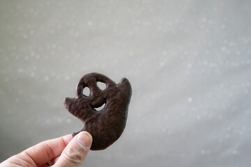 a smiling happy Halloween ghost cookie held with one hand on a gray background with star glitter and copy space