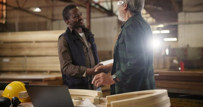 Teamwork, laptop in workshop and handshake, apprentice and designer furniture manufacturing. Mentorship, carpentry and men at sustainable business, teaching and learning with computer for job project