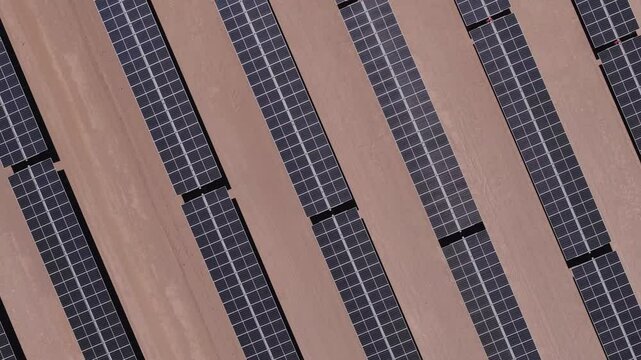 drone captura uma vista a&eacute;rea de um parque solar no deserto, exibindo c&eacute;lulas fotovoltaicas e m&oacute;dulos solares sob o c&eacute;u ensolarado