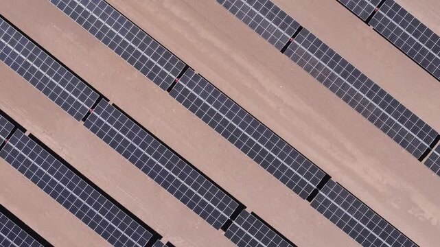 drone captura uma vista a&eacute;rea de um parque solar no deserto, exibindo c&eacute;lulas fotovoltaicas e m&oacute;dulos solares sob o c&eacute;u ensolarado