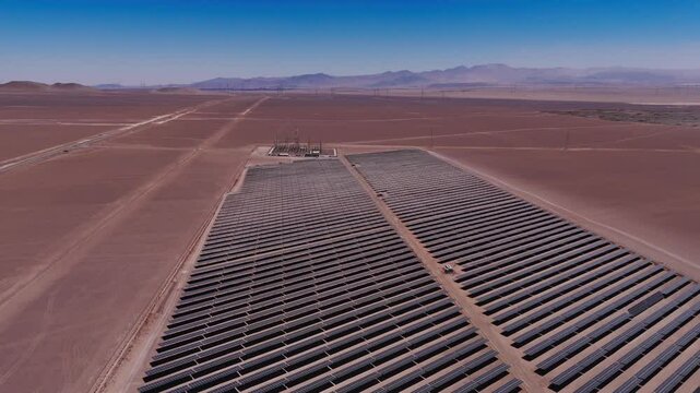 drone captura uma vista a&eacute;rea de um parque solar no deserto, exibindo c&eacute;lulas fotovoltaicas e m&oacute;dulos solares sob o c&eacute;u ensolarado