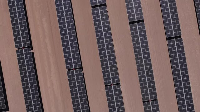 drone captura uma vista a&eacute;rea de um parque solar no deserto, exibindo c&eacute;lulas fotovoltaicas e m&oacute;dulos solares sob o c&eacute;u ensolarado