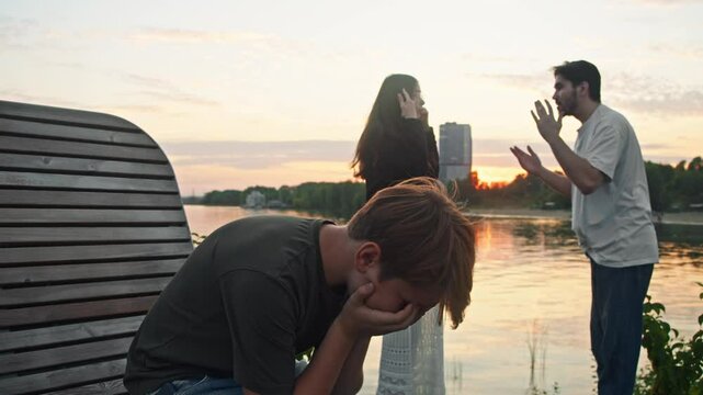 Husband and wife are arguing loudly and angrily in a public setting, while their son covers his eyes in embarrassment and begins to cry.