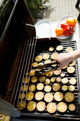 Grilling fresh eggplant and bell peppers outdoors on a sunny day in a backyard setting
