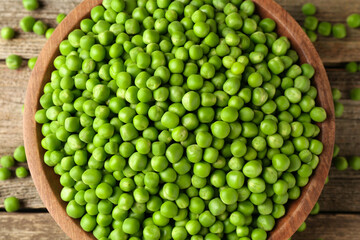 Fresh green peas in bowl on wooden table, top view