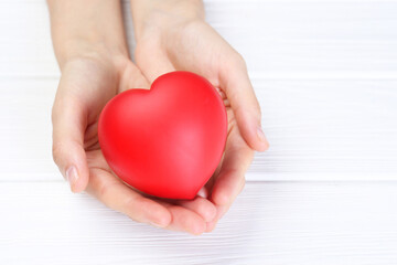 Woman holding red heart at white wooden table, closeup