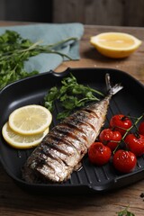 Delicious grilled mackerel, tomatoes, parsley and lemon in pan on wooden table, closeup