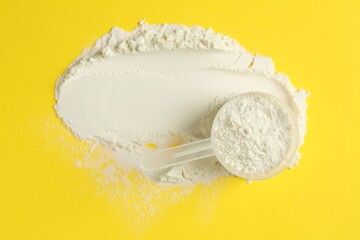 Protein powder and scoop on yellow background, top view