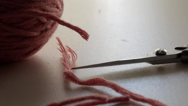 slight camera movement close to a pastel coloured wool - strings of wool and a pair of scissors lie on the table