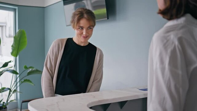 Woman patient talking receptionist at healthcare appointment. Smiling client