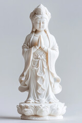 Naklejka premium Elegant white statue of Kwan Yin with hands pressed together in a prayer gesture, dressed in flowing robes, on a lotus flower base.