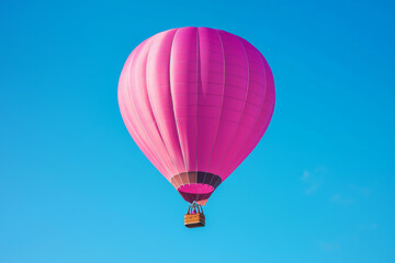 Fototapeta premium A vibrant pink hot air balloon floats against a clear blue sky, symbolizing adventure and leisure.