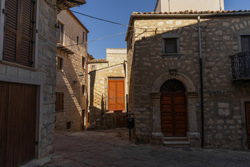 Narrow alley between stone buildings with wooden shutters. Sunlight creates dramatic shadows in this rustic European village