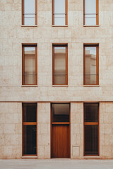 A minimalist building facade made of beige brick with large wooden windows and a brown door, featuring intricate geometric patterns on the wall, straight lines, and modern architecture