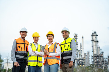 Group of Asian engineer people with safety helmet standing front of oil refinery. Industry zone gas petrochemical. Factory oil storage tank and pipeline. Workers team work in refinery construction