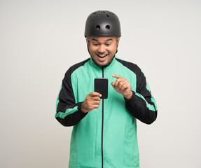 Young asian rider wearing green jacket uniform and bike helmet standing holding smartphone food application on isolated. Male delivery service worker. Delivery courier and shipping food service.