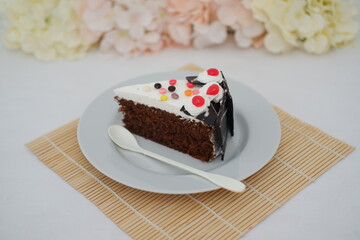 A piece of cake on a white plate with a spoon on a bamboo mat