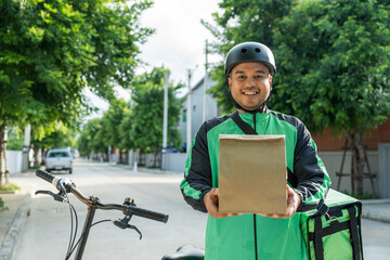 Obraz premium Portrait Rider food delivery man wearing green uniform and helmet cycling a bicycle the food service to customer. Happy delivery man with green backpack shipping of goods to customers.