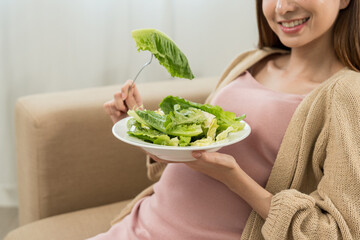 Happy pregnant woman eating vegetable salad and smiling to camera, concept of healthy mother taking health care and nourish her fetal and waiting her childbirth.