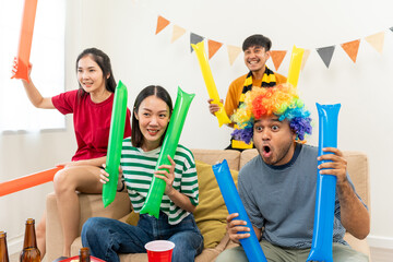 Group of asian friends man and woman watching cheering football match on TV at home. Eating snack...