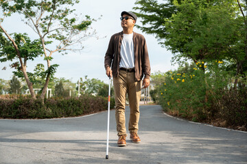 Young blind man walking in city with walking stick. Visually impaired man difficult to traveling on the road wearing sun glasses Cross the road cross the footbridge