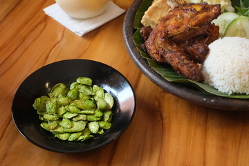 a plate of food with rice, vegetables, grilled chicken and fried petai. served on a plate covered with typical Indonesian banana leaves
