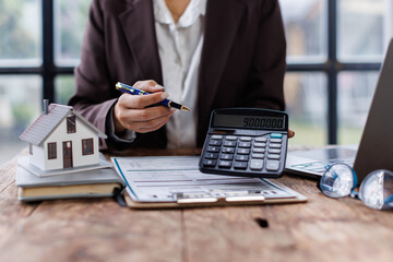 Pressing calculators, hand plans home refinance. House model, buy or rent, calculators on desk. Saving for property purchase, optimal mortgage payment. Tax, credit analysis for financial planning.

