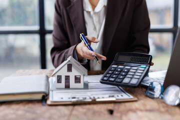 Pressing calculators, hand plans home refinance. House model, buy or rent, calculators on desk. Saving for property purchase, optimal mortgage payment. Tax, credit analysis for financial planning.
