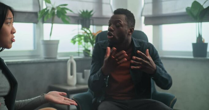 Aggressive African American man loses self control, starts fight and yells at his Asian girlfriend during couples therapy. Multiethnic young family having quarrel on counseling session with therapist.