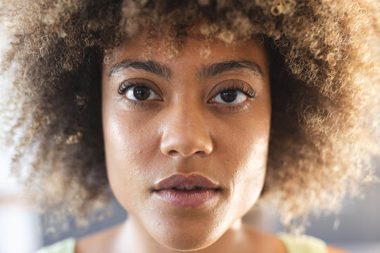 Close-up portrait of woman with curly hair, looking directly at camera, at home