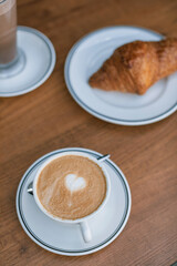 Overhead view of a cup of delicious cappuccino and a fresh croissant on a plate on a wooden table