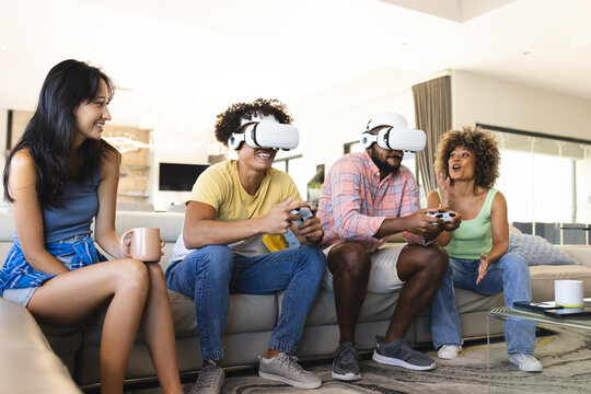 Playing video games with VR headsets, diverse friends enjoying time together on couch, at home