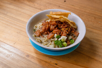 a bowl of chicken noodles, or mie ayam, on a wooden table