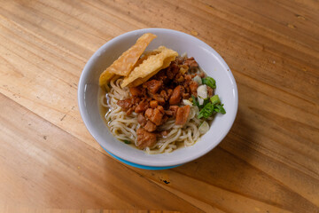 a bowl of chicken noodles, or mie ayam, on a wooden table