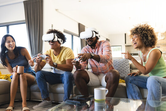 Playing video games with VR headsets, diverse friends enjoying time together on couch, at home