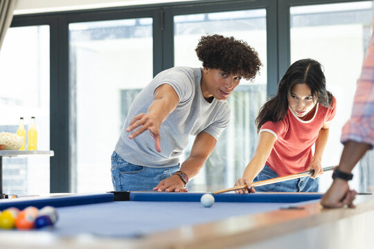 Playing pool, diverse friends aiming and focusing on billiard table during hangout, at home