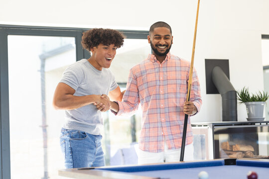Playing pool, two diverse friends enjoying leisure time and smiling together indoors, at home