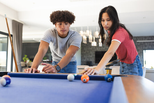 Playing pool, diverse friends focusing on making shots on billiards table indoors, at home